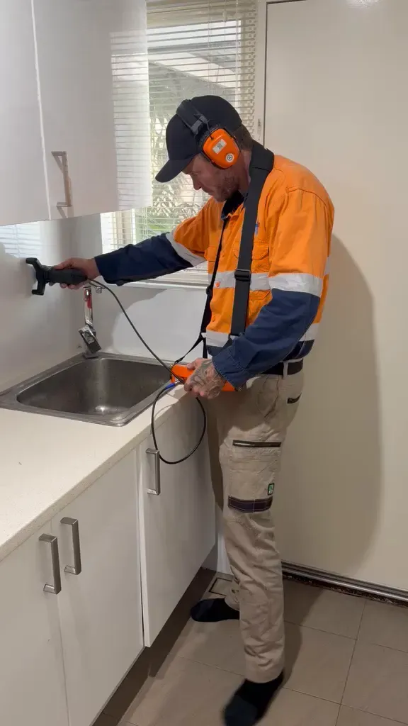 Leak detection technician tracing a hidden leak under a kitchen sink